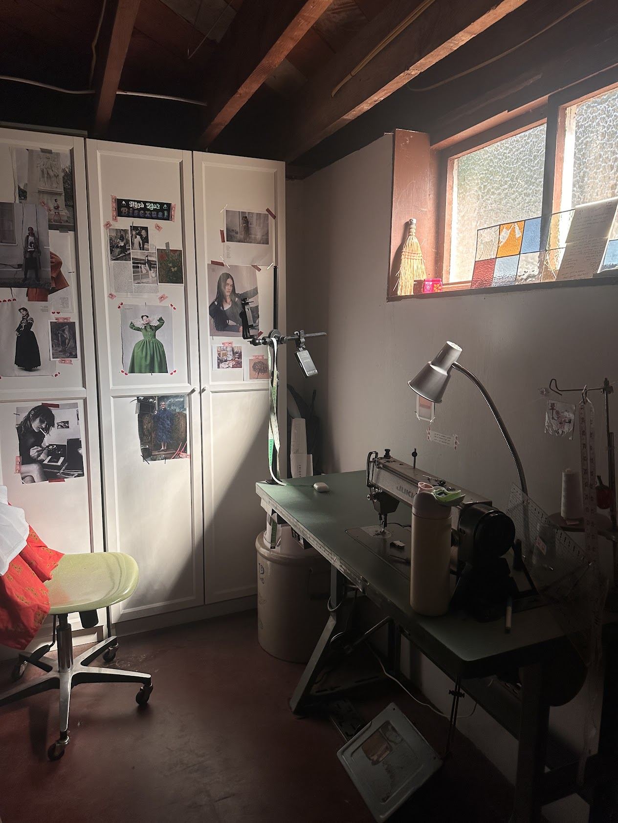 A basement sewing studio with a work table and lamp under exposed ceiling joists